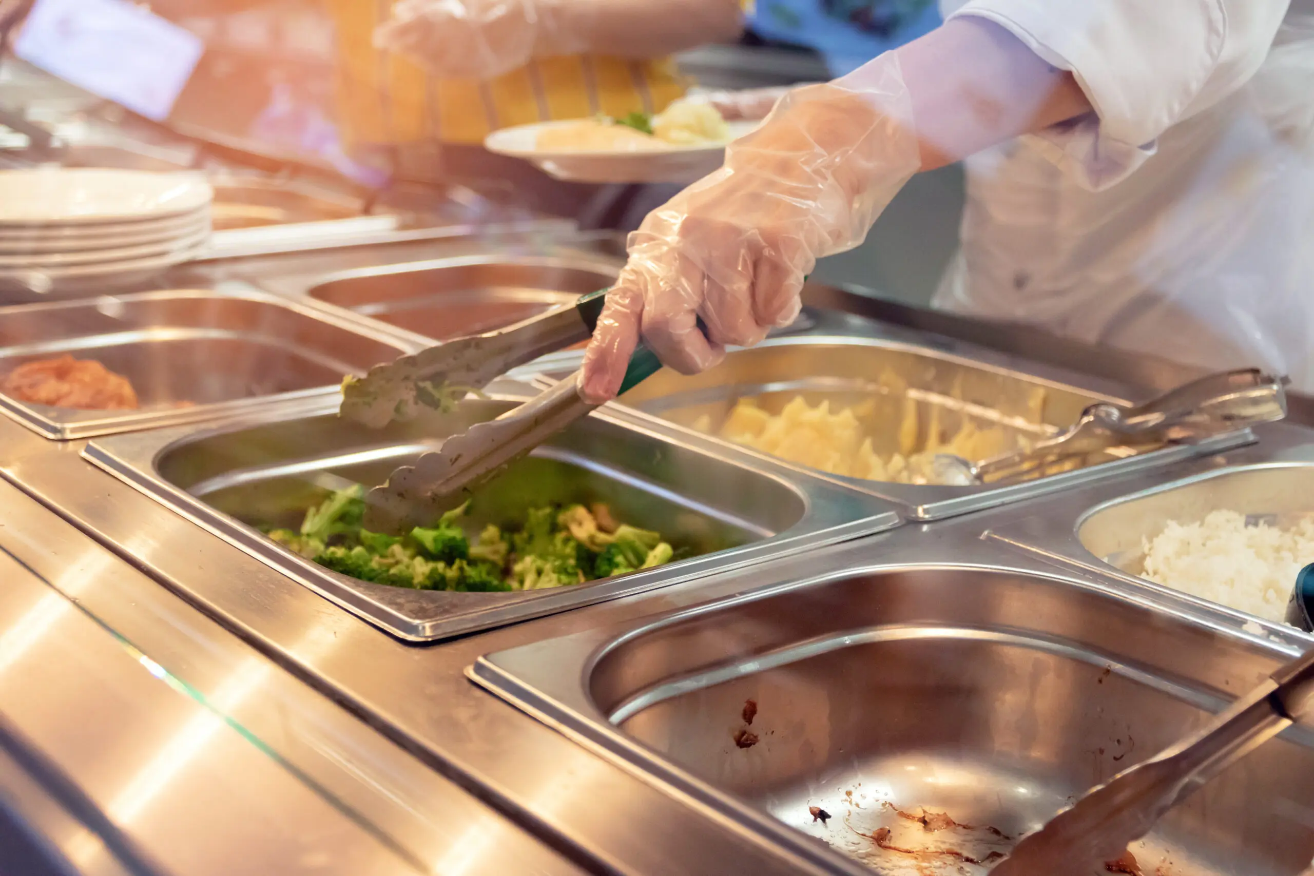Cafeteria staff serving food from a hot line