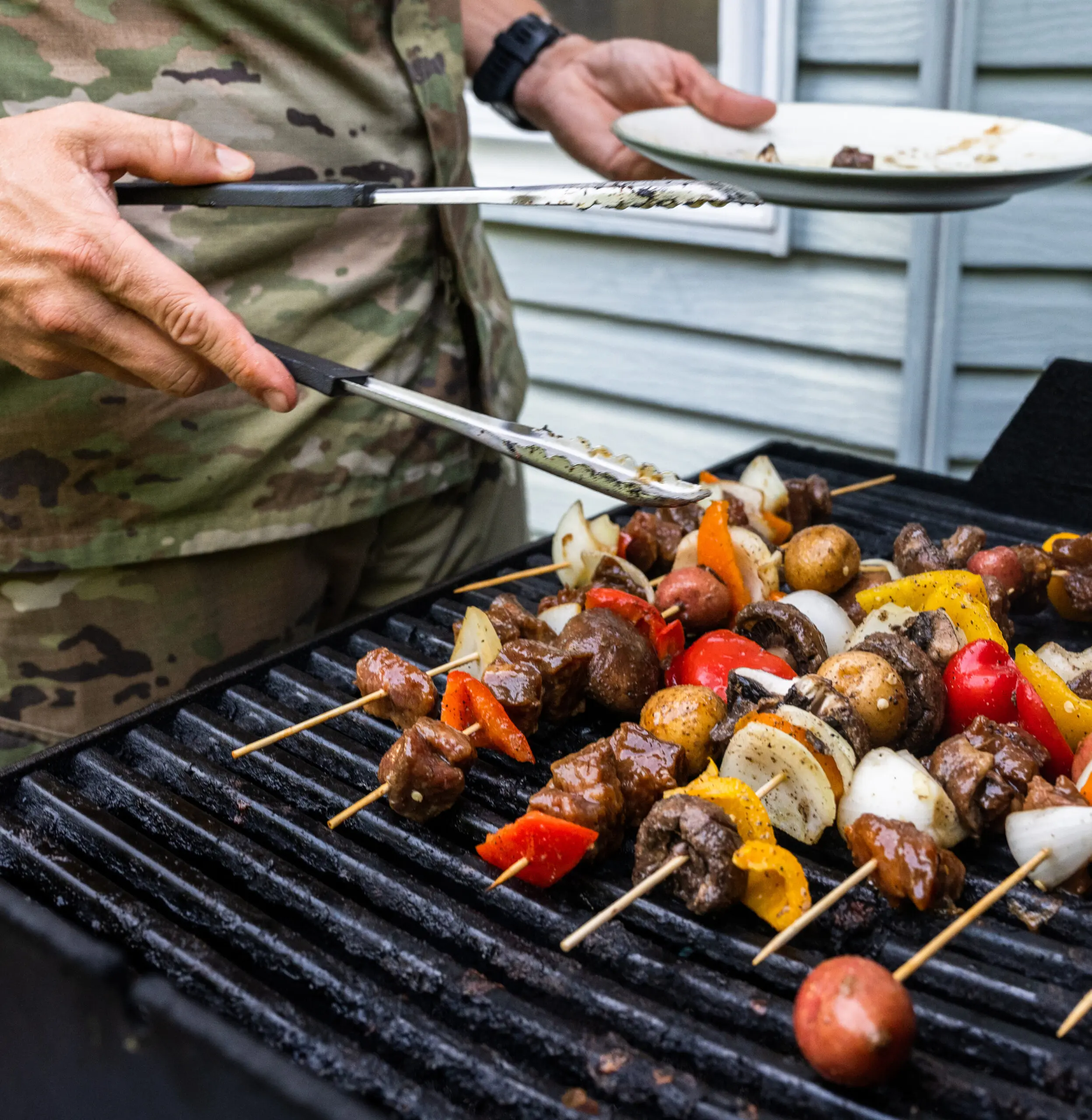 Military servicemember grills kebabs on base.