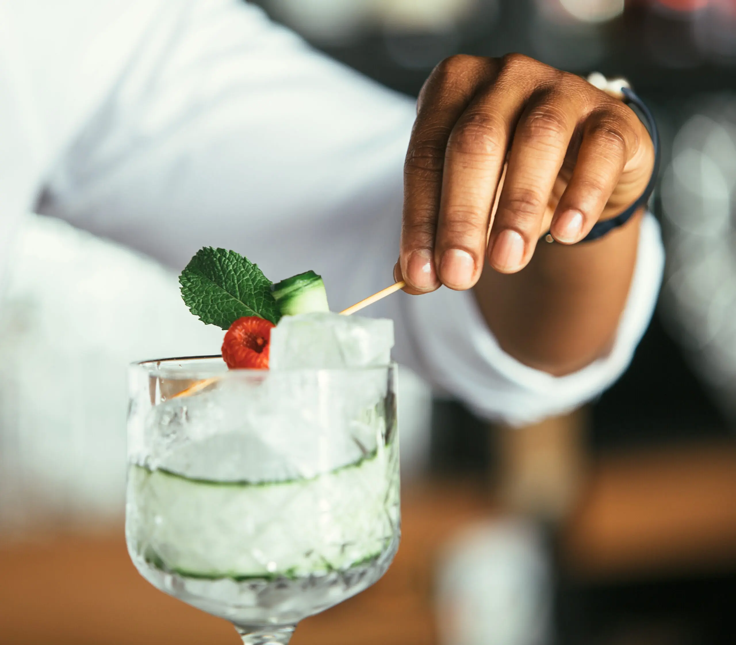 Hand garnishing a crafted cocktail with ice and herbs