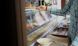 Corporate employee selecting a hot meal from office cafeteria serving line.