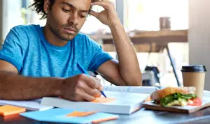 Student studying at a table with a sandwich and coffee.